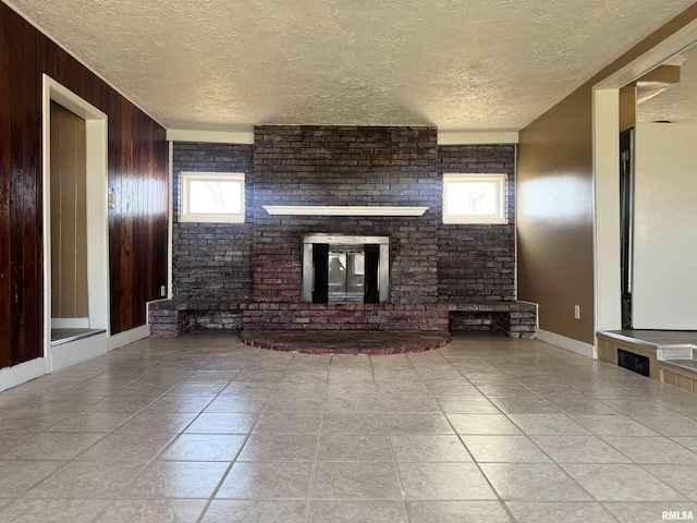 unfurnished living room featuring tile patterned floors, wooden walls, a brick fireplace, and a textured ceiling