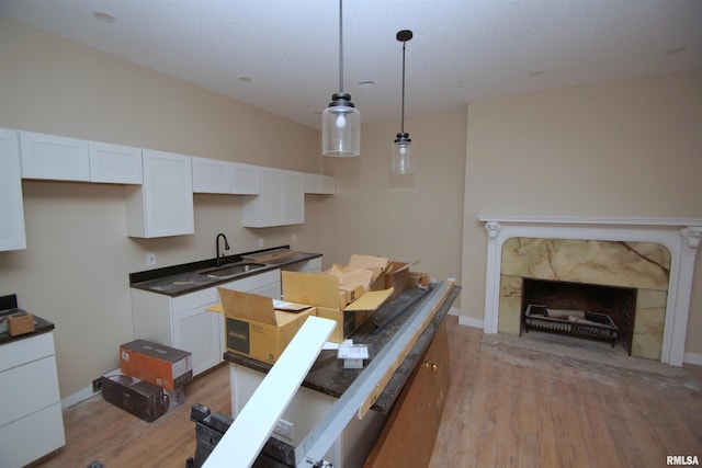 kitchen featuring decorative light fixtures, light wood-type flooring, white cabinetry, and sink