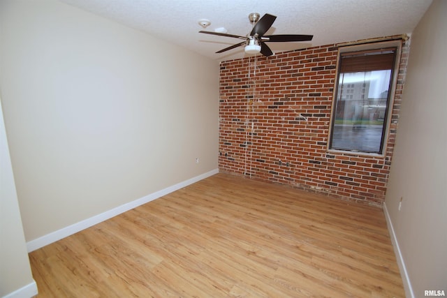 unfurnished room with a textured ceiling, light hardwood / wood-style floors, and brick wall