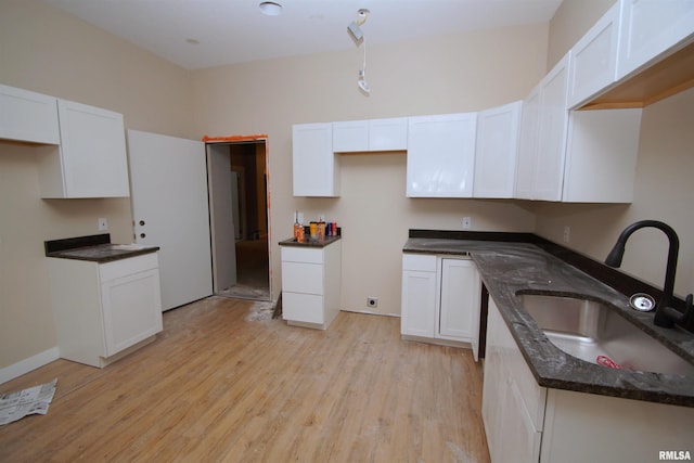 kitchen with white cabinetry, sink, dark stone counters, and light hardwood / wood-style flooring