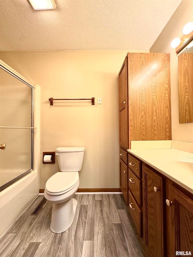 full bathroom featuring bath / shower combo with glass door, a textured ceiling, vanity, hardwood / wood-style flooring, and toilet