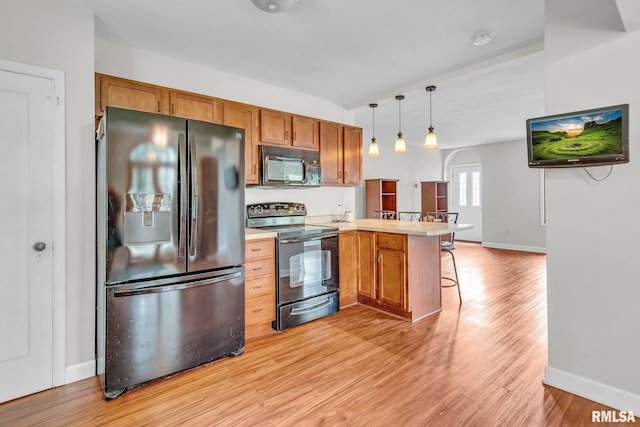 kitchen with black appliances, decorative light fixtures, light hardwood / wood-style floors, kitchen peninsula, and a breakfast bar area