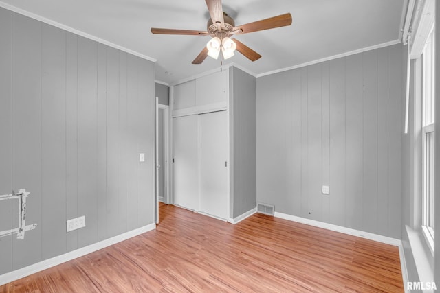 unfurnished bedroom with ceiling fan, light hardwood / wood-style flooring, wooden walls, and ornamental molding