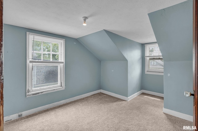 additional living space featuring a textured ceiling, light colored carpet, and lofted ceiling