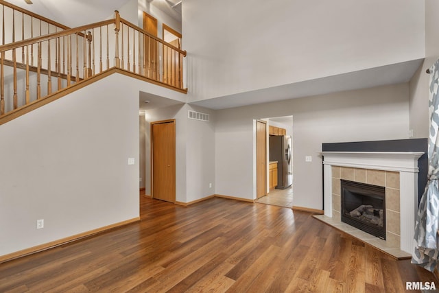 unfurnished living room featuring wood-type flooring, a high ceiling, and a tiled fireplace