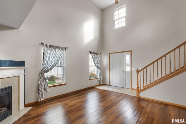 entrance foyer with a tile fireplace, hardwood / wood-style floors, and a towering ceiling