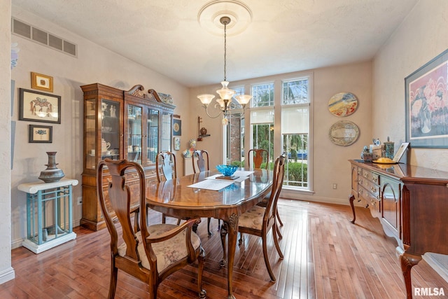 dining space with a textured ceiling, light hardwood / wood-style floors, and an inviting chandelier