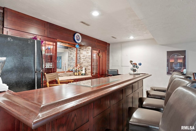 bar with wooden walls, black appliances, and a textured ceiling