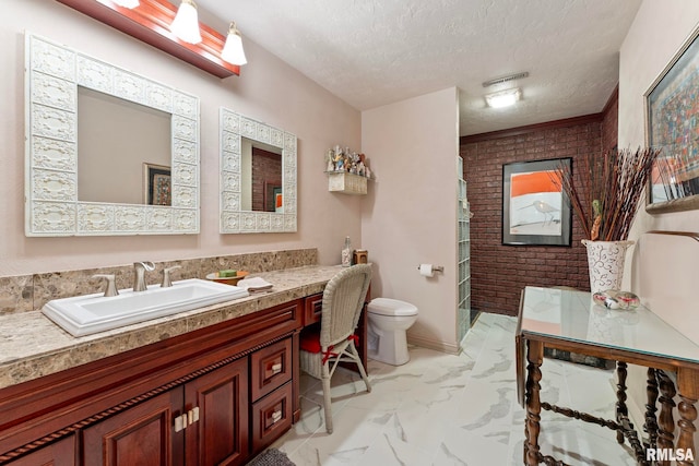 bathroom featuring vanity, toilet, a textured ceiling, and brick wall