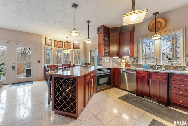 kitchen with stone counters, dishwasher, sink, decorative light fixtures, and black oven