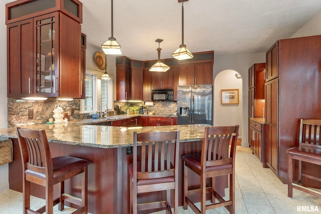 kitchen with stainless steel refrigerator with ice dispenser, backsplash, light stone counters, and hanging light fixtures