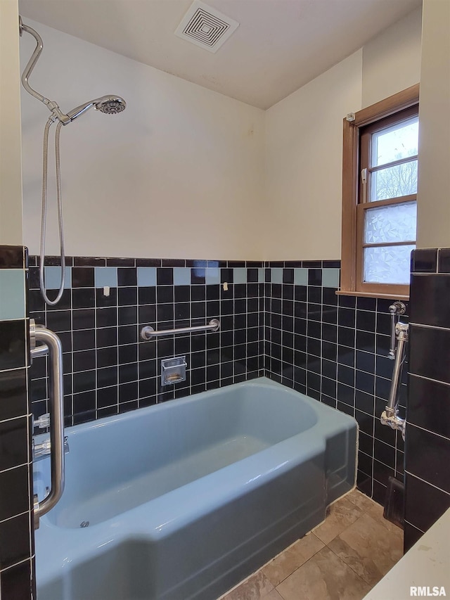 bathroom with a tub to relax in, tile patterned flooring, and tile walls