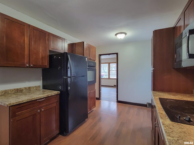 kitchen with hardwood / wood-style floors, light stone counters, and black appliances