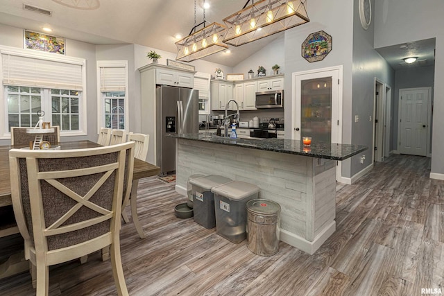 kitchen featuring pendant lighting, dark stone counters, a kitchen bar, wood-type flooring, and stainless steel appliances