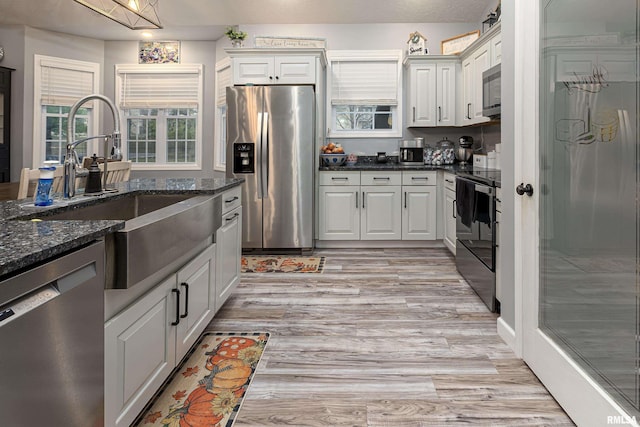 kitchen featuring dark stone counters, stainless steel appliances, sink, light hardwood / wood-style floors, and white cabinetry