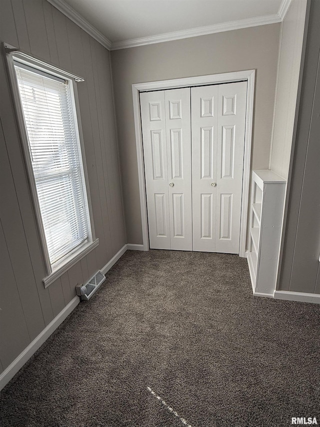 unfurnished bedroom with ornamental molding, a closet, and dark colored carpet