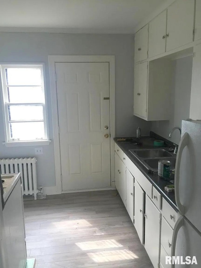 kitchen featuring radiator heating unit, dark countertops, freestanding refrigerator, and white cabinets