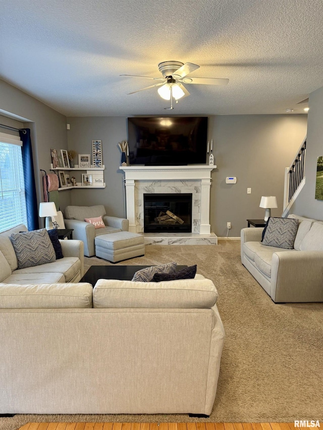 carpeted living room with ceiling fan, a textured ceiling, and a high end fireplace