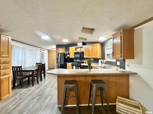 kitchen featuring kitchen peninsula, light wood-type flooring, crown molding, sink, and black appliances