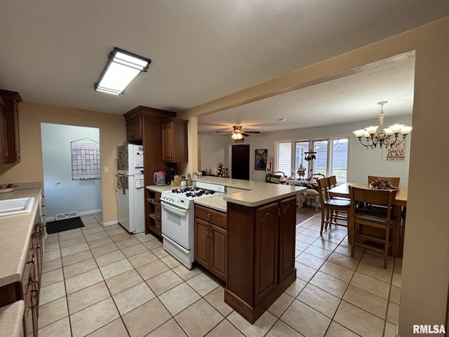 kitchen with kitchen peninsula, ceiling fan with notable chandelier, white appliances, sink, and light tile patterned floors