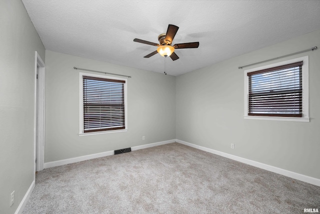 empty room with ceiling fan, light colored carpet, and a textured ceiling