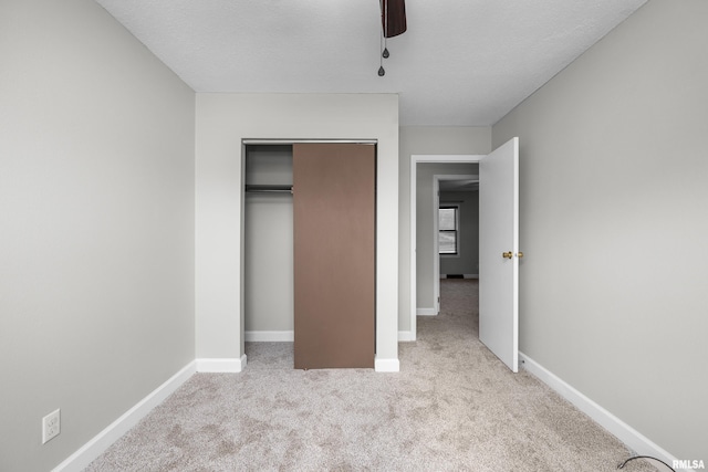 unfurnished bedroom featuring a textured ceiling, a closet, light colored carpet, and ceiling fan