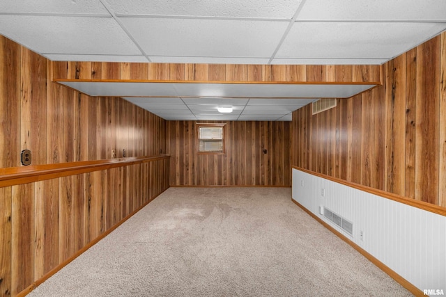 basement featuring wooden walls, a drop ceiling, and carpet floors