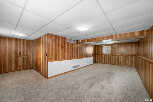 basement with light colored carpet, a drop ceiling, and wood walls