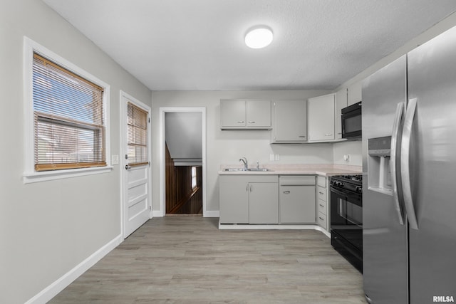 kitchen featuring light wood-type flooring, a textured ceiling, sink, and black appliances