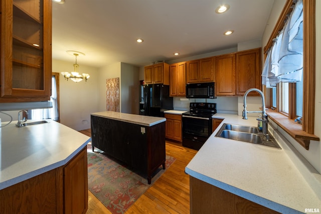 kitchen with an inviting chandelier, black appliances, sink, hardwood / wood-style flooring, and a kitchen island