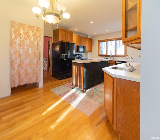 kitchen featuring black appliances, decorative light fixtures, sink, and light hardwood / wood-style flooring