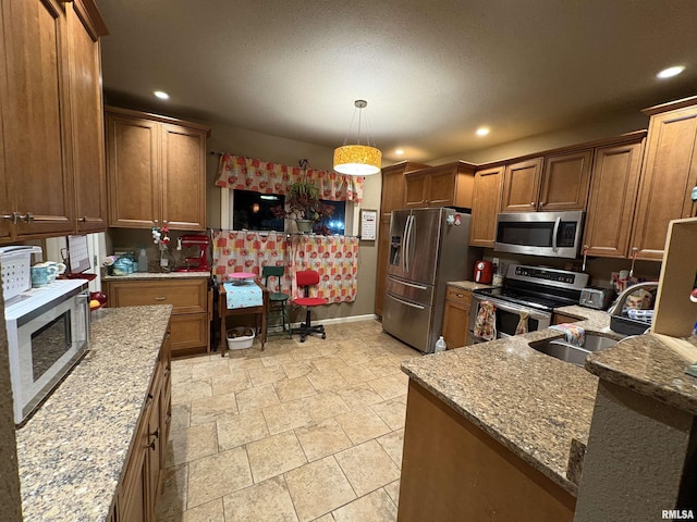 kitchen featuring light stone counters, sink, decorative light fixtures, and appliances with stainless steel finishes