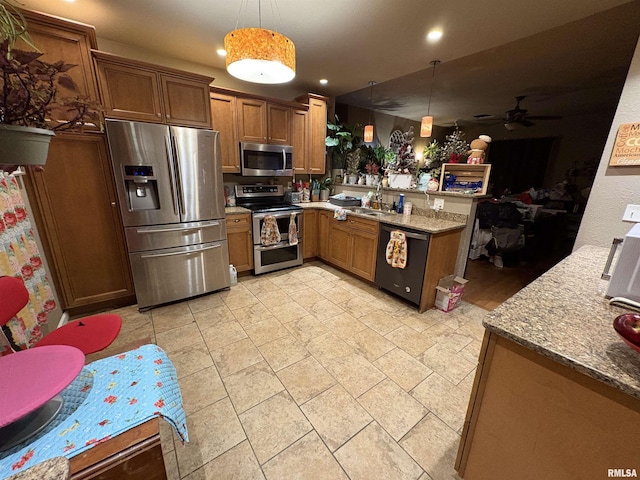 kitchen featuring sink, light stone counters, kitchen peninsula, pendant lighting, and stainless steel appliances