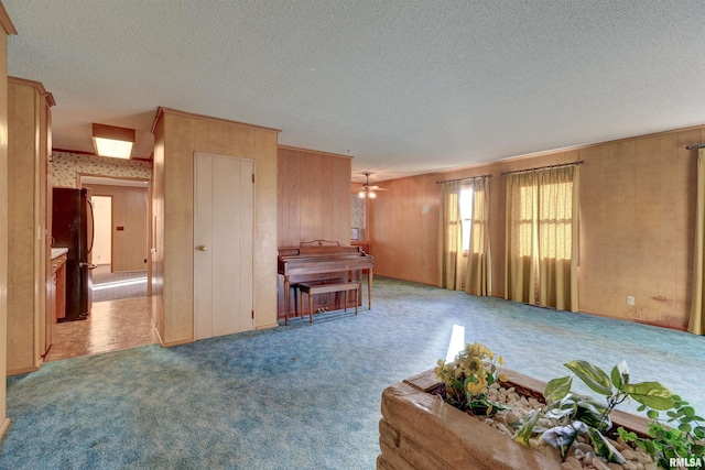 unfurnished living room with a textured ceiling, light carpet, ceiling fan, and wood walls