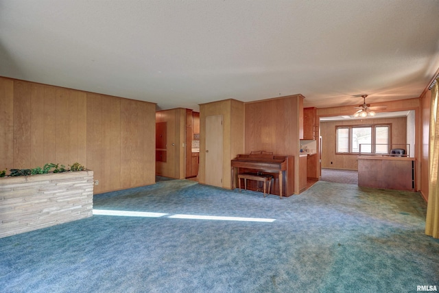 unfurnished living room with wooden walls, carpet floors, and ceiling fan