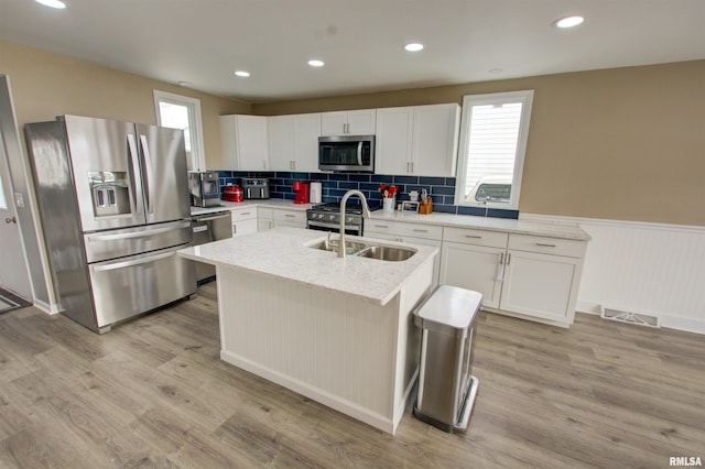 kitchen with a sink, light wood-style floors, a wainscoted wall, and stainless steel appliances