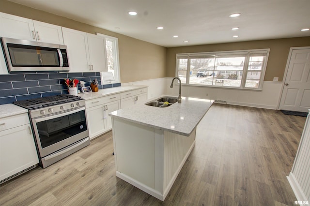 kitchen with a sink, white cabinetry, light wood finished floors, and stainless steel appliances