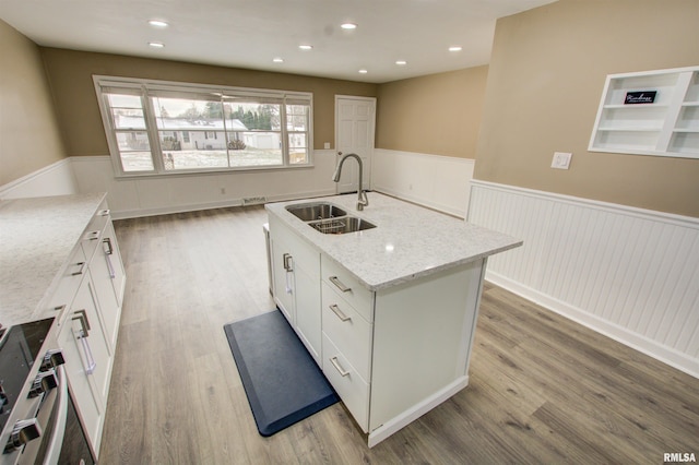 kitchen with a wainscoted wall, a sink, white cabinets, range, and light wood-type flooring