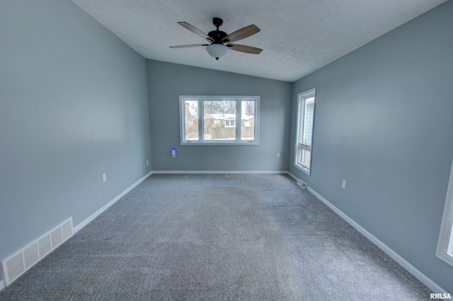 carpeted empty room with visible vents, a textured ceiling, baseboards, ceiling fan, and vaulted ceiling