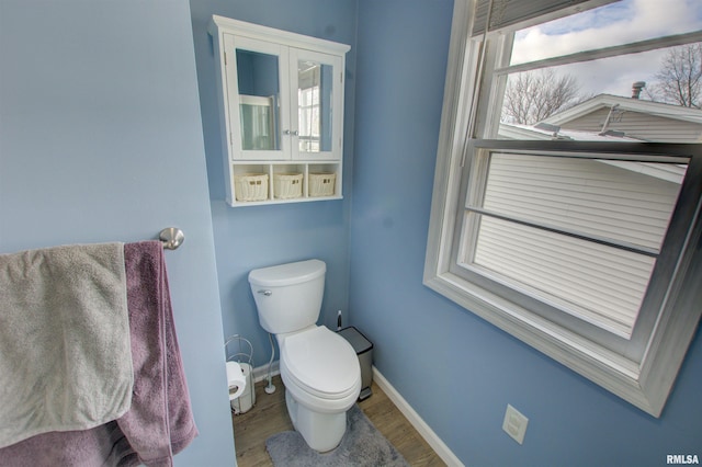 bathroom with baseboards, plenty of natural light, toilet, and wood finished floors