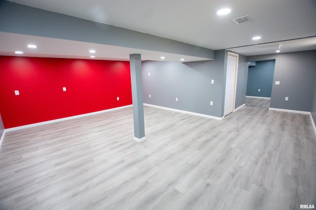 finished below grade area featuring visible vents, an accent wall, baseboards, and wood finished floors