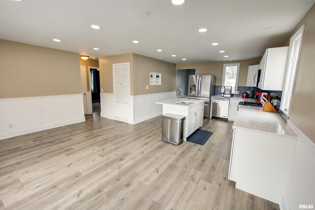 kitchen featuring a wainscoted wall, a center island with sink, a sink, appliances with stainless steel finishes, and light wood-type flooring