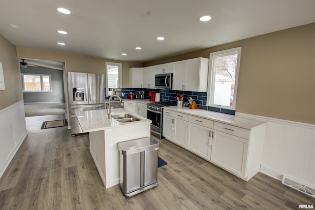 kitchen with wood finished floors, a sink, stainless steel appliances, white cabinets, and wainscoting