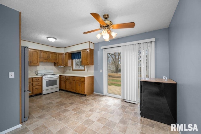 kitchen featuring stainless steel refrigerator, gas range gas stove, ceiling fan, and a textured ceiling