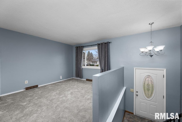 carpeted entryway featuring a textured ceiling and an inviting chandelier