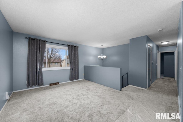 carpeted empty room featuring a notable chandelier and a textured ceiling