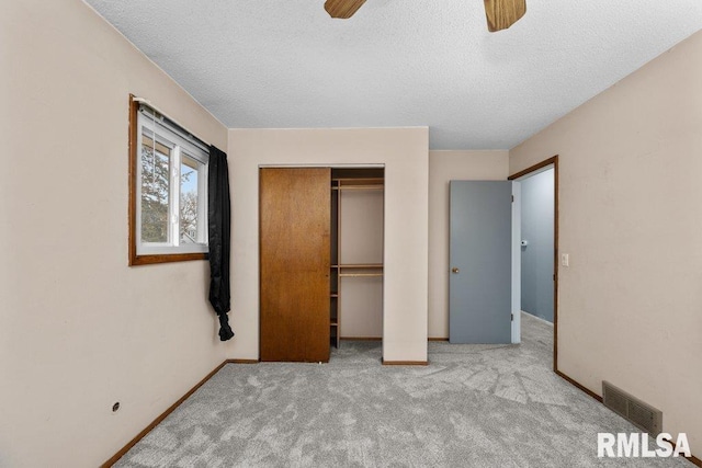 unfurnished bedroom with a textured ceiling, ceiling fan, light carpet, and a closet