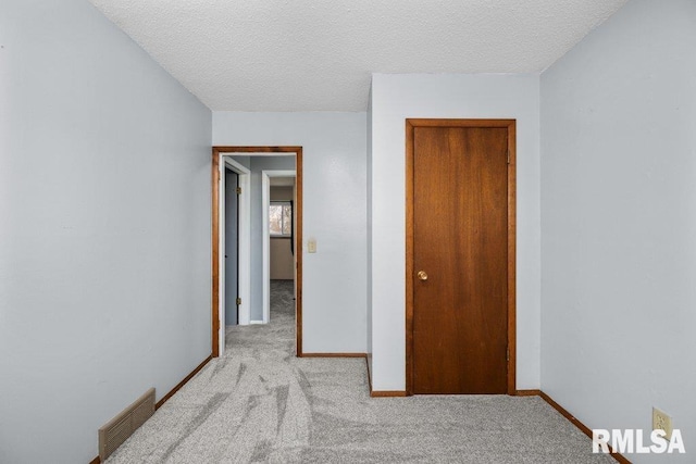 unfurnished bedroom featuring a textured ceiling, light carpet, and a closet