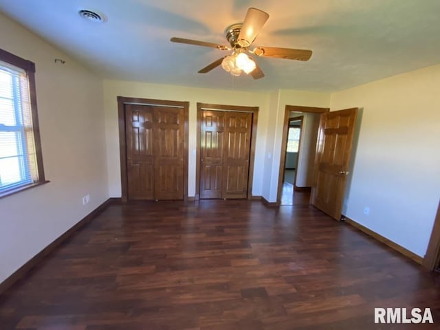 unfurnished bedroom with multiple closets, dark wood-type flooring, and ceiling fan