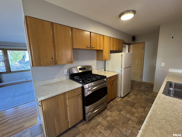 kitchen with white refrigerator, stainless steel gas range oven, dark wood-type flooring, and sink